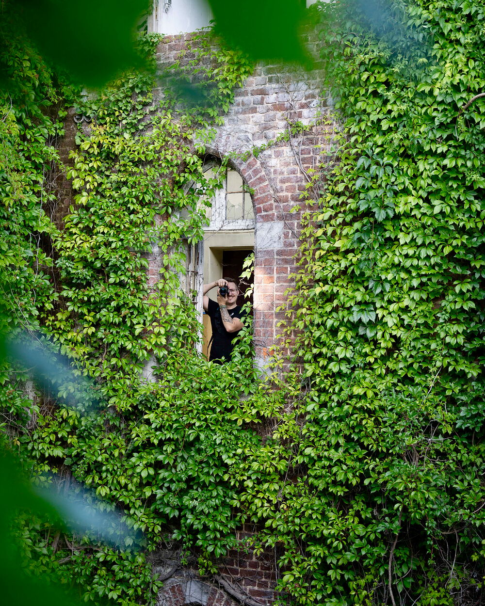 Lenny Obez photographing from an ivy-clad window in an abandoned building