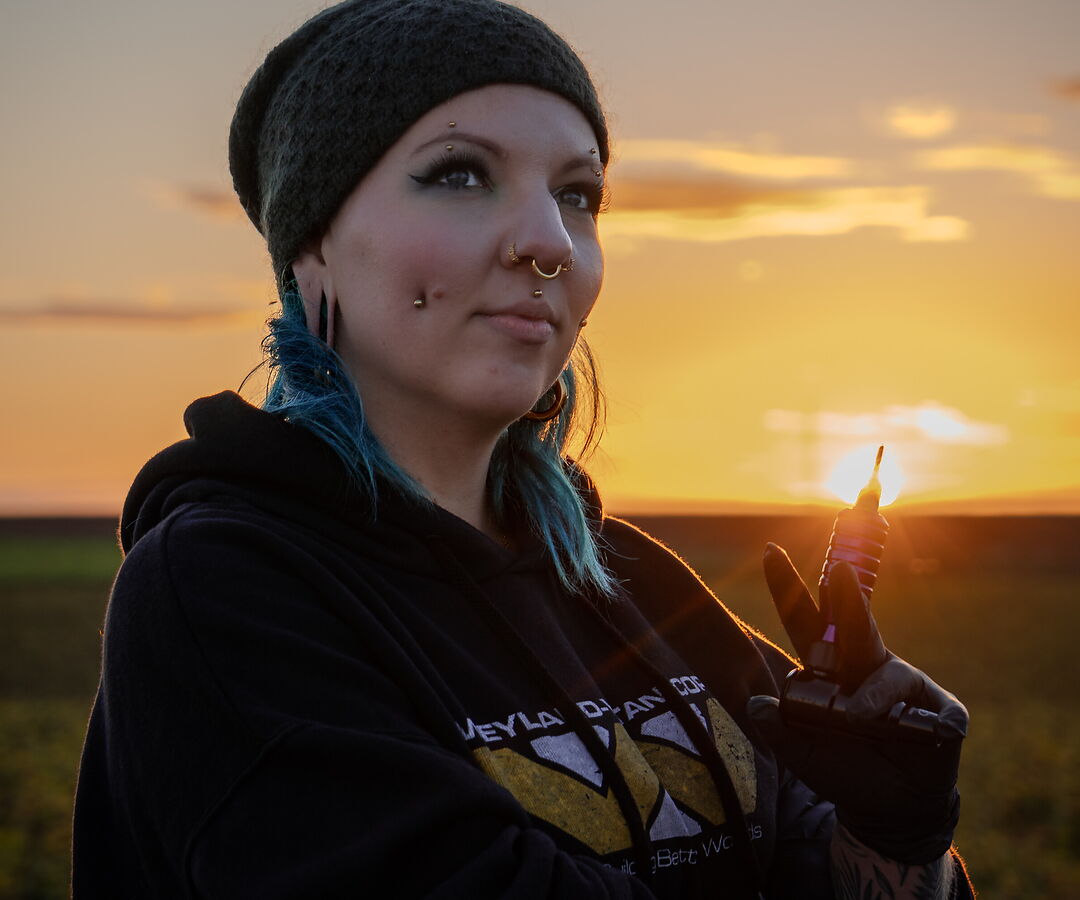 Golden-hour portrait of Sophie Guiot (Spooky So), tattoo artist, near a wind turbine in Hesbaye